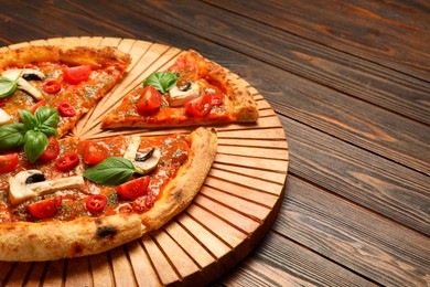 Tasty pizza with basil, mushrooms, chili pepper and tomato on wooden table, closeup. Space for text