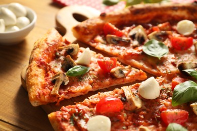 Tasty pizza with basil, mushrooms, mozzarella and tomato on wooden table, closeup