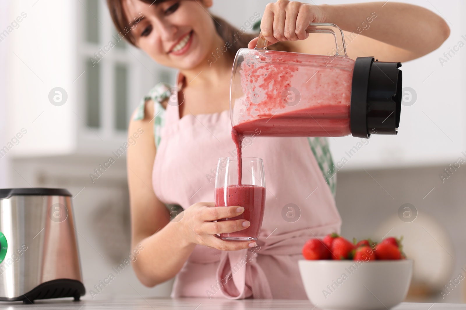 Photo of Woman pouring fresh smoothie from blender cup into glass in kitchen, selective focus