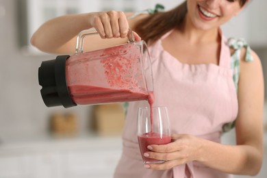 Photo of Woman pouring fresh smoothie from blender cup into glass in kitchen, closeup