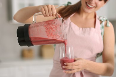 Woman pouring fresh smoothie from blender cup into glass in kitchen, closeup