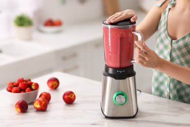 Woman making delicious smoothie with blender at white marble table in kitchen, closeup