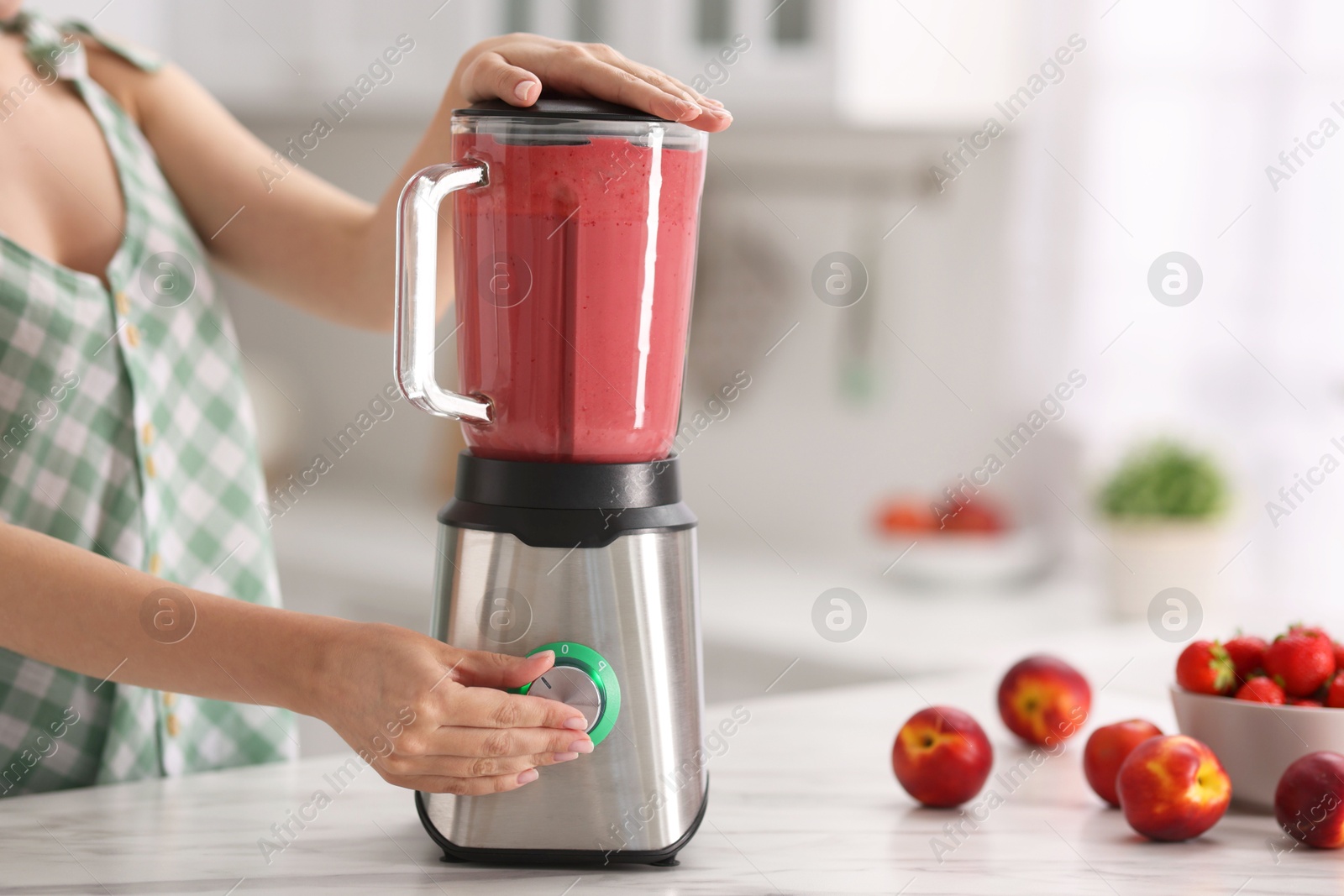 Photo of Woman making delicious smoothie with blender at white marble table in kitchen, closeup