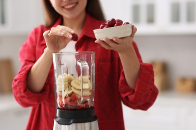 Woman making delicious smoothie with blender in kitchen, closeup