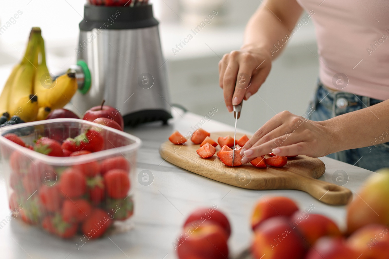 Photo of Woman cutting strawberry for smoothie at white marble table in kitchen, closeup