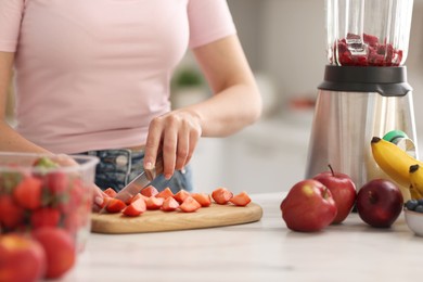 Woman making delicious smoothie with blender at white marble table in kitchen, closeup