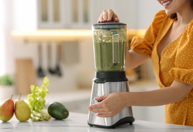 Woman making delicious smoothie with blender at white marble table in kitchen, closeup