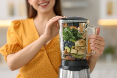 Woman making delicious smoothie with blender in kitchen, closeup