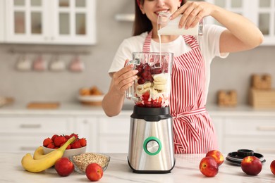 Woman making delicious smoothie with blender at white marble table in kitchen, closeup