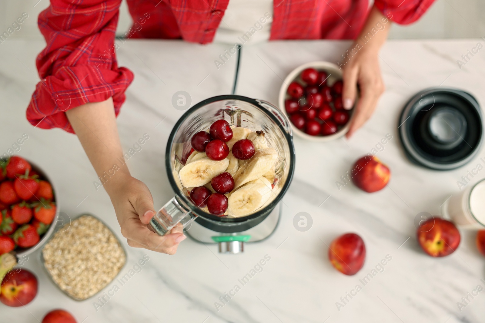 Photo of Woman making delicious smoothie with blender at white marble table in kitchen, above view