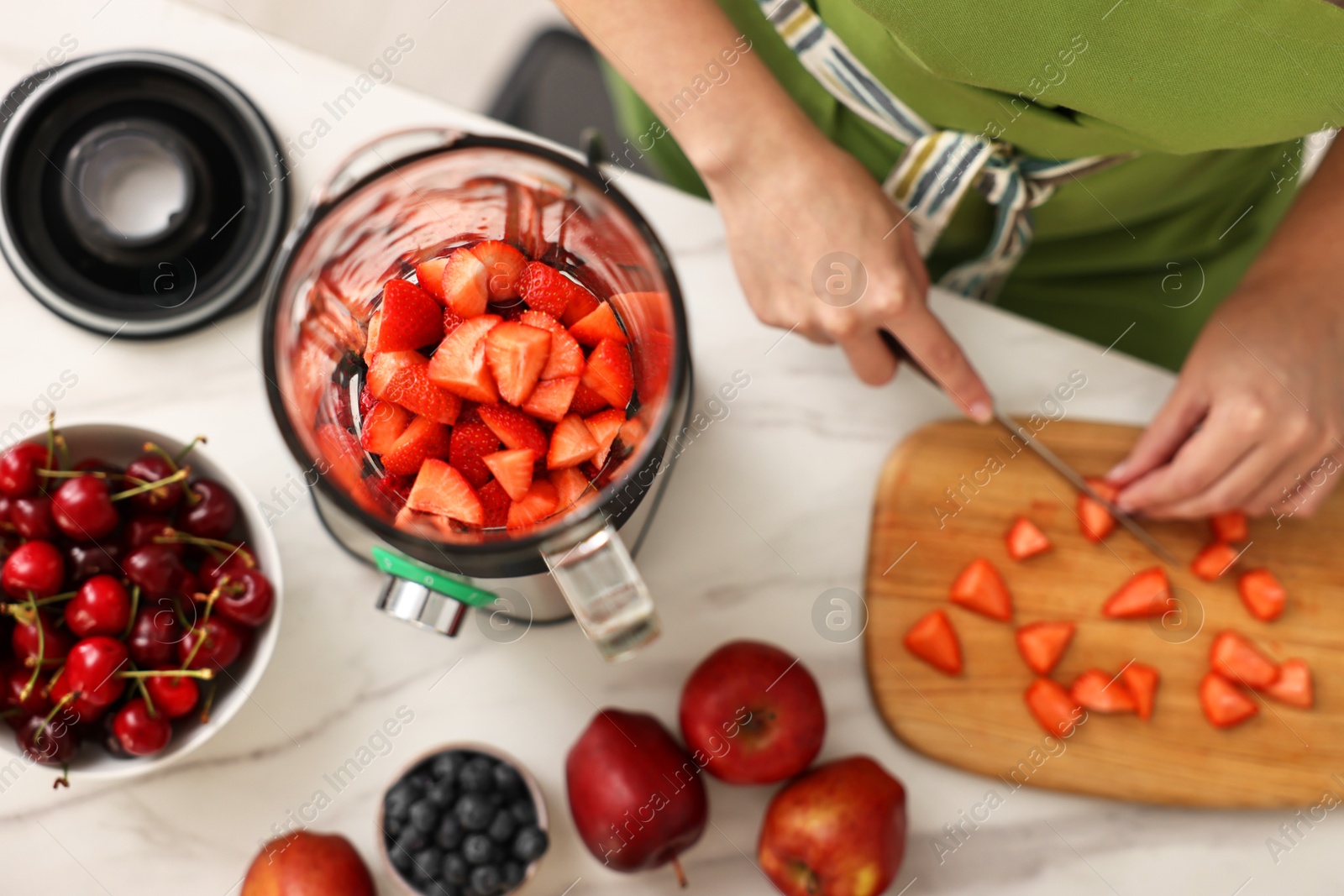 Photo of Woman making delicious smoothie with blender at white marble table in kitchen, top view