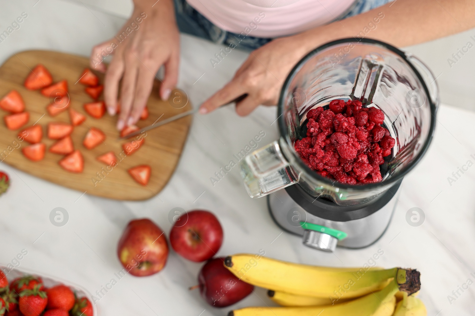 Photo of Woman making delicious smoothie with blender at white marble table in kitchen, above view