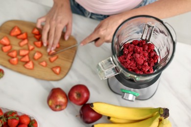 Woman making delicious smoothie with blender at white marble table in kitchen, above view