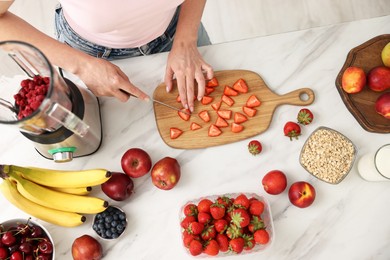 Photo of Woman making delicious smoothie with blender at white marble table in kitchen, above view