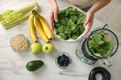 Woman making delicious smoothie with blender at white marble table in kitchen, top view