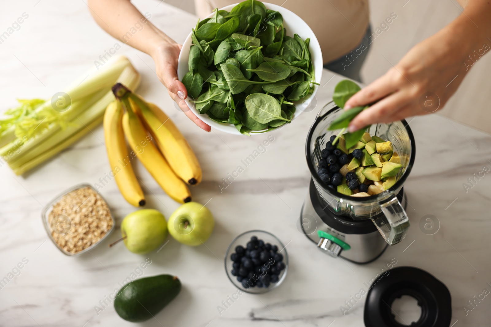 Photo of Woman making delicious smoothie with blender at white marble table in kitchen, above view