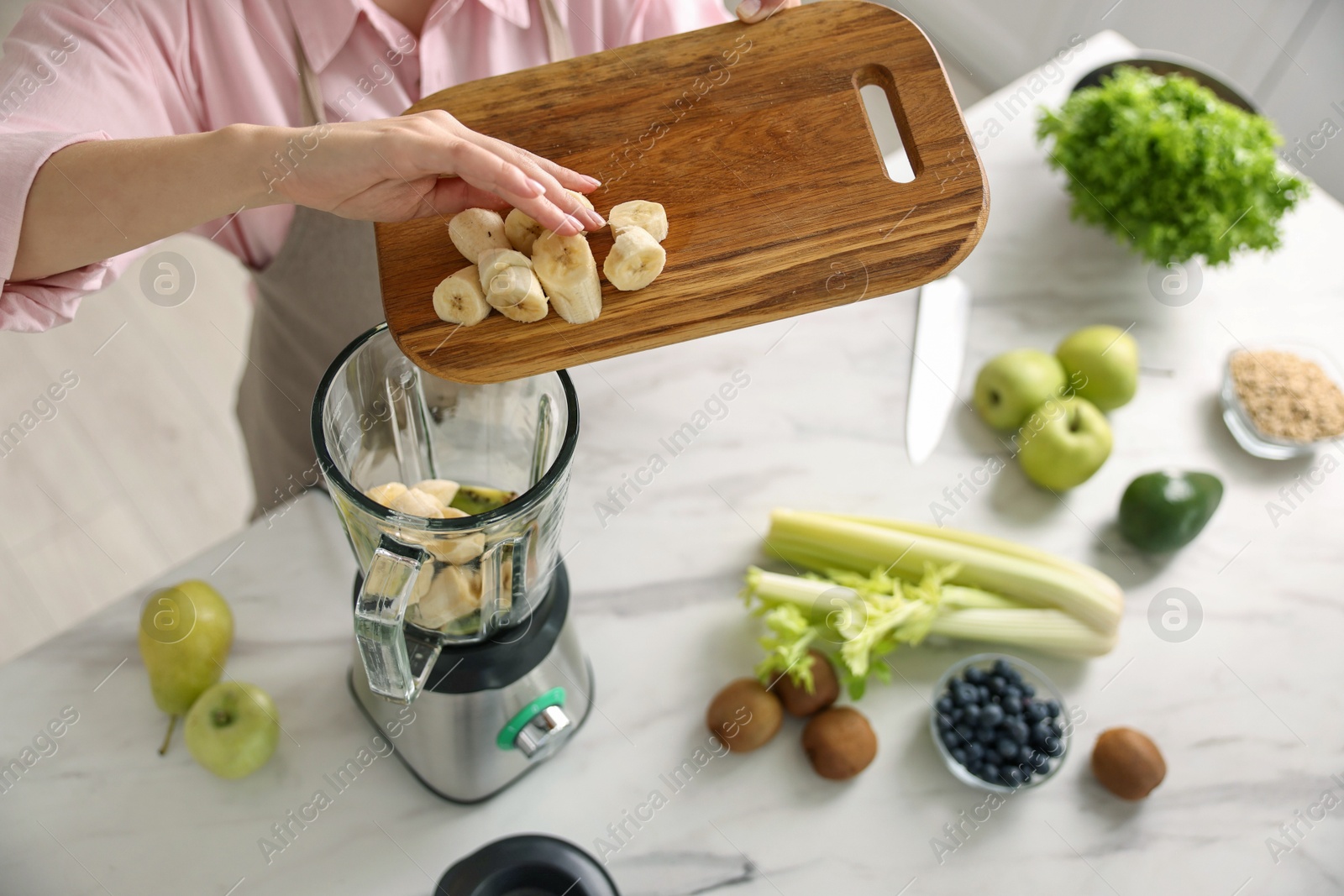 Photo of Woman making delicious smoothie with blender at white marble table in kitchen, above view