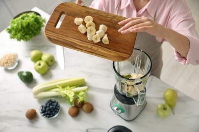 Photo of Woman making delicious smoothie with blender at white marble table in kitchen, above view