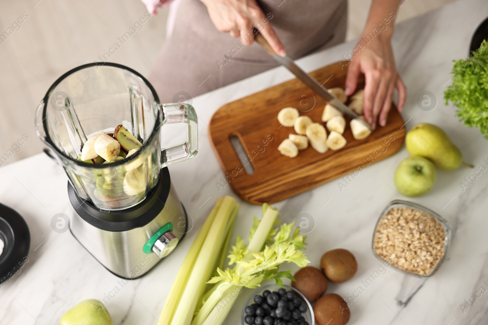 Photo of Woman making delicious smoothie with blender at white marble table in kitchen, closeup