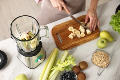 Woman making delicious smoothie with blender at white marble table in kitchen, closeup