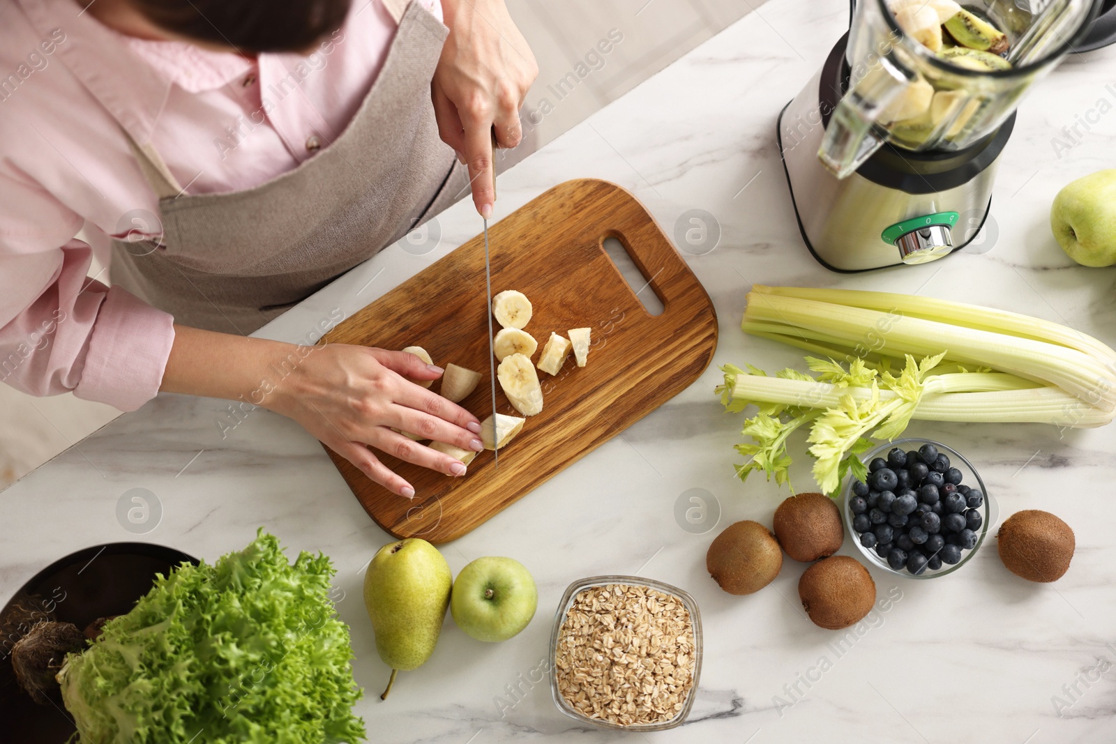 Photo of Woman making delicious smoothie with blender at white marble table in kitchen, above view