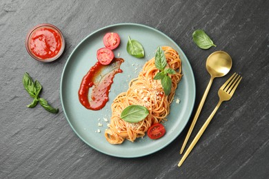 Photo of Delicious pasta with tomato sauce, basil and cheese served on black textured table, flat lay