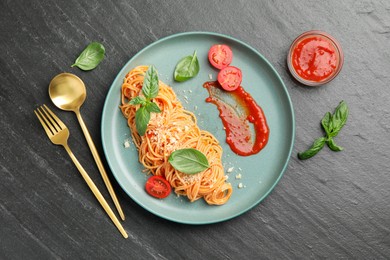 Delicious pasta with tomato sauce, basil and cheese served on black textured table, flat lay