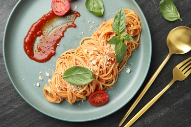 Photo of Delicious pasta with tomato sauce, basil and cheese served on black textured table, flat lay