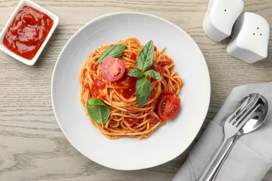 Photo of Delicious pasta with tomato sauce and basil in bowl served on wooden table, flat lay