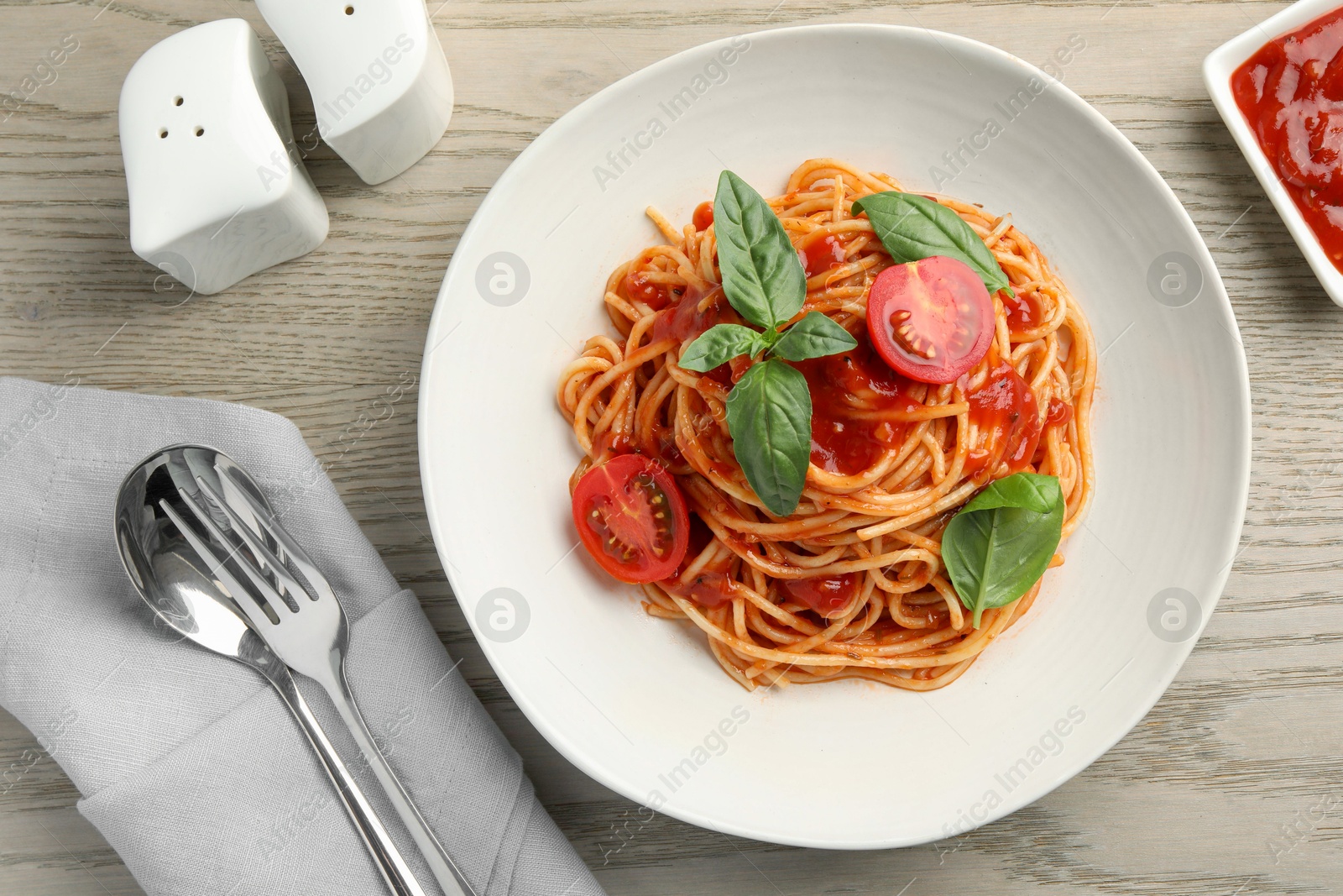 Photo of Delicious pasta with tomato sauce and basil in bowl served on wooden table, flat lay