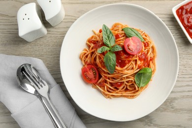 Delicious pasta with tomato sauce and basil in bowl served on wooden table, flat lay