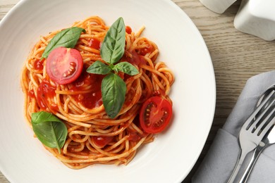 Delicious pasta with tomato sauce and basil in bowl served on wooden table, flat lay