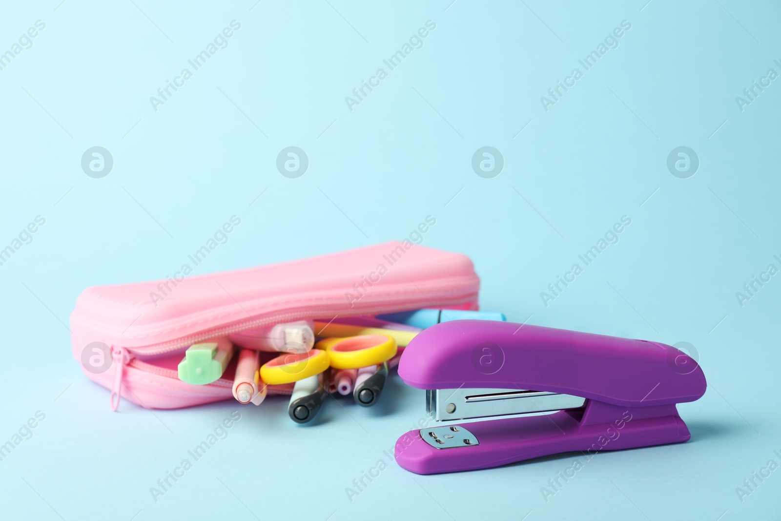 Photo of Violet stapler and other stationery on light blue background, closeup