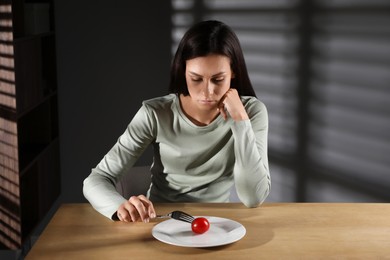 Photo of Eating disorder. Sad woman with fork near tomato at wooden table