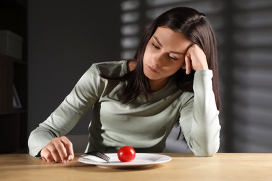 Eating disorder. Sad woman with fork near tomato at wooden table