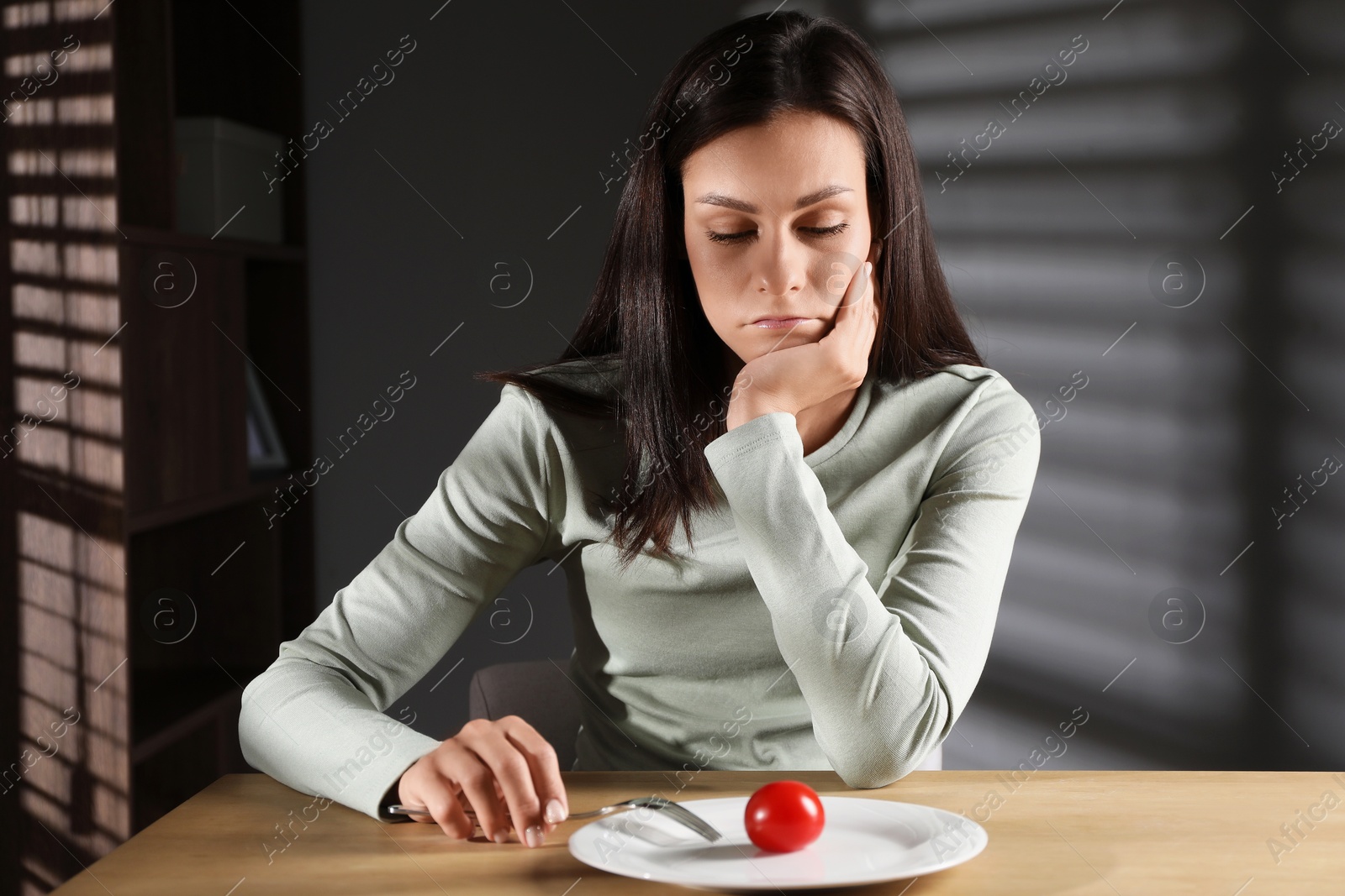 Photo of Eating disorder. Sad woman with fork near tomato at wooden table