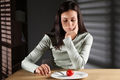 Photo of Eating disorder. Sad woman with fork near tomato at wooden table