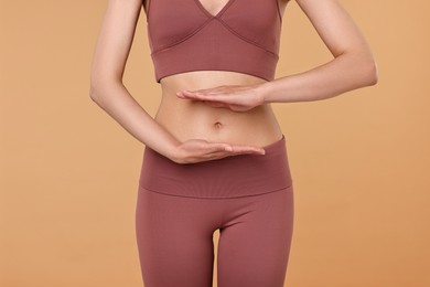 Photo of Healthy digestion. Woman holding something near her belly on beige background, closeup