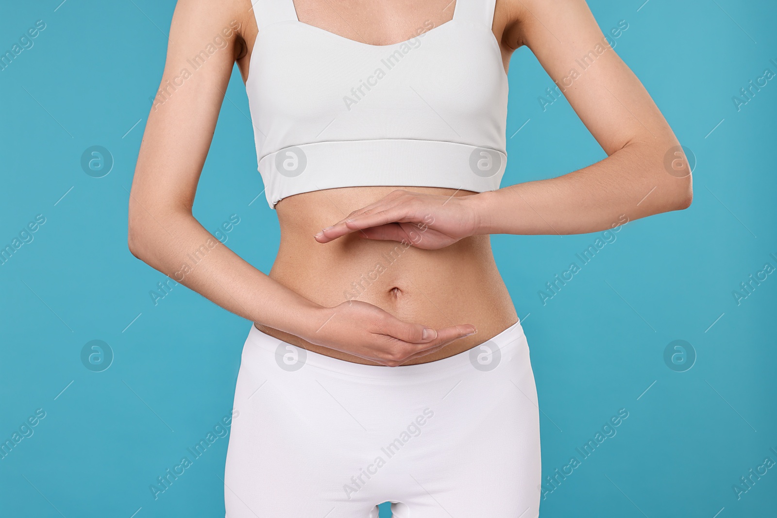 Photo of Healthy digestion. Woman holding something near her belly on light blue background, closeup