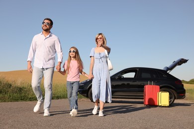 Photo of Parents, their daughter, car and suitcases outdoors. Family traveling