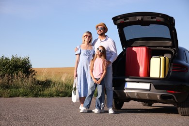 Happy family near car with suitcases outdoors, space for text