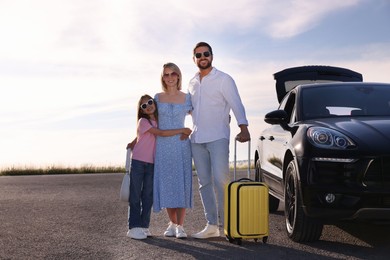 Happy family with suitcase near car outdoors, space for text