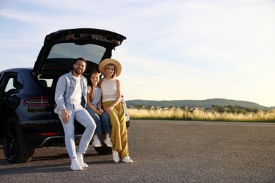 Happy family sitting in trunk of car outdoors, space for text