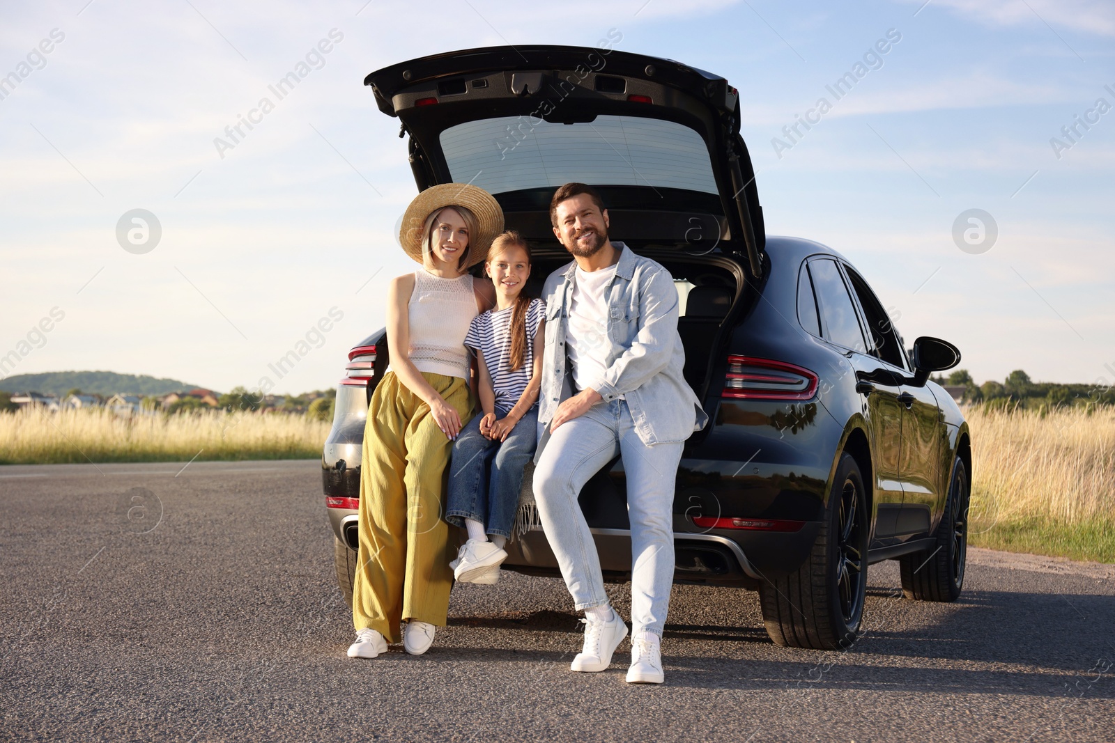 Photo of Happy family sitting in trunk of car outdoors