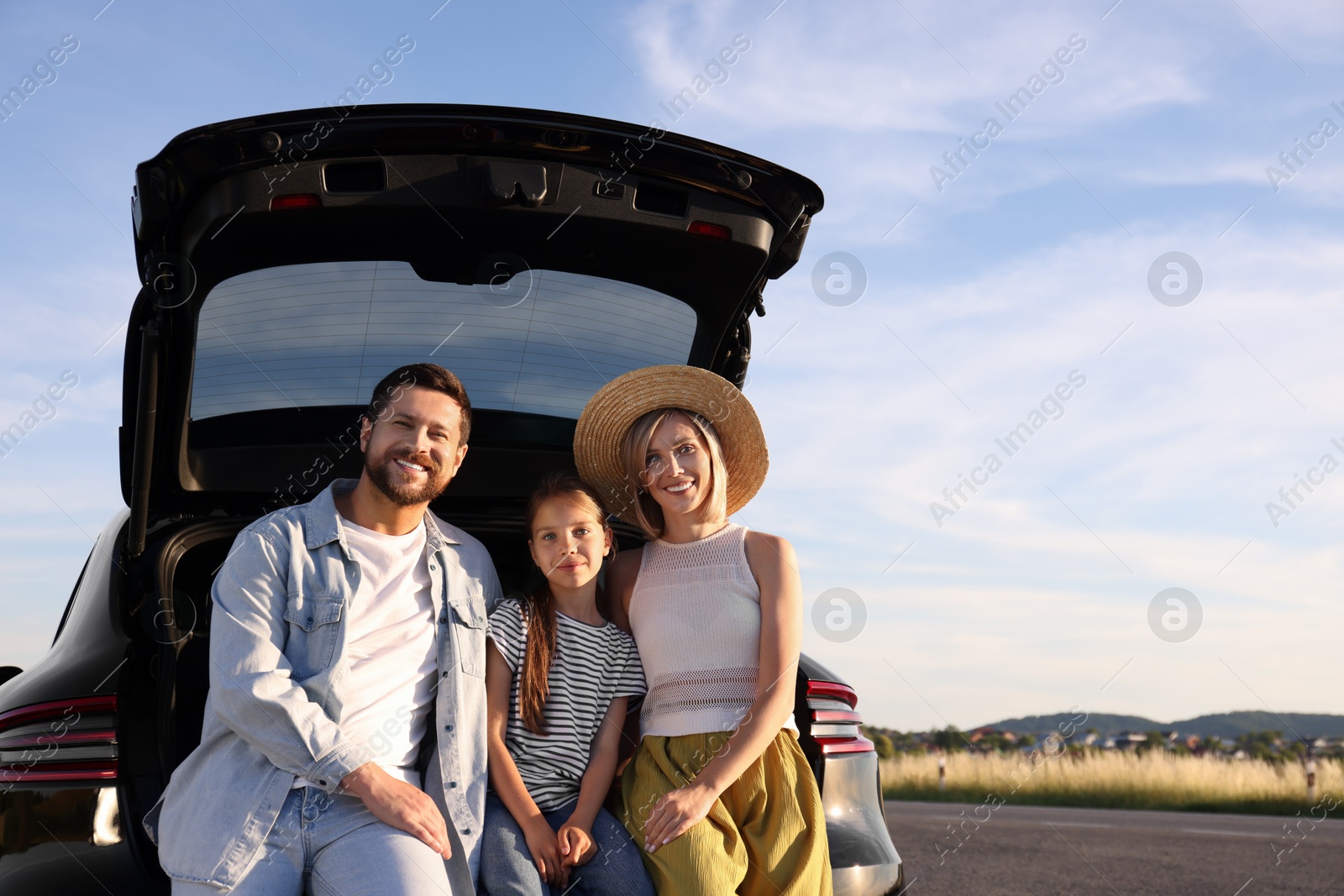 Photo of Happy family sitting in trunk of car outdoors, space for text