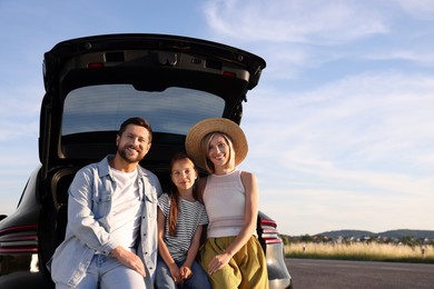 Happy family sitting in trunk of car outdoors, space for text