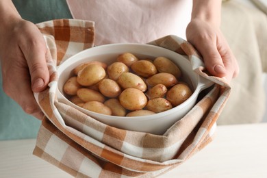 Woman holding pot with raw potatoes at table, closeup