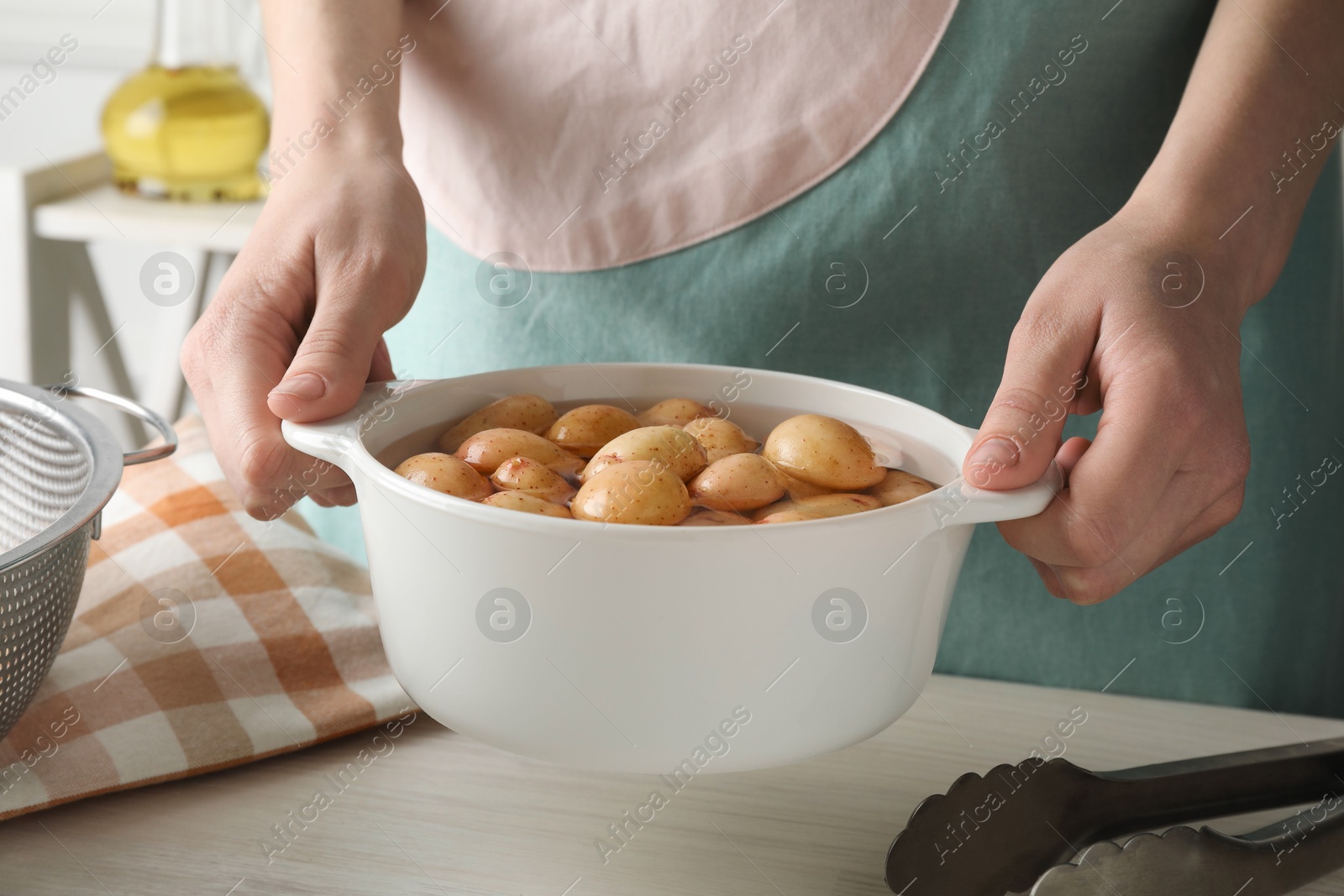 Photo of Woman holding pot with raw potatoes at white wooden table, closeup