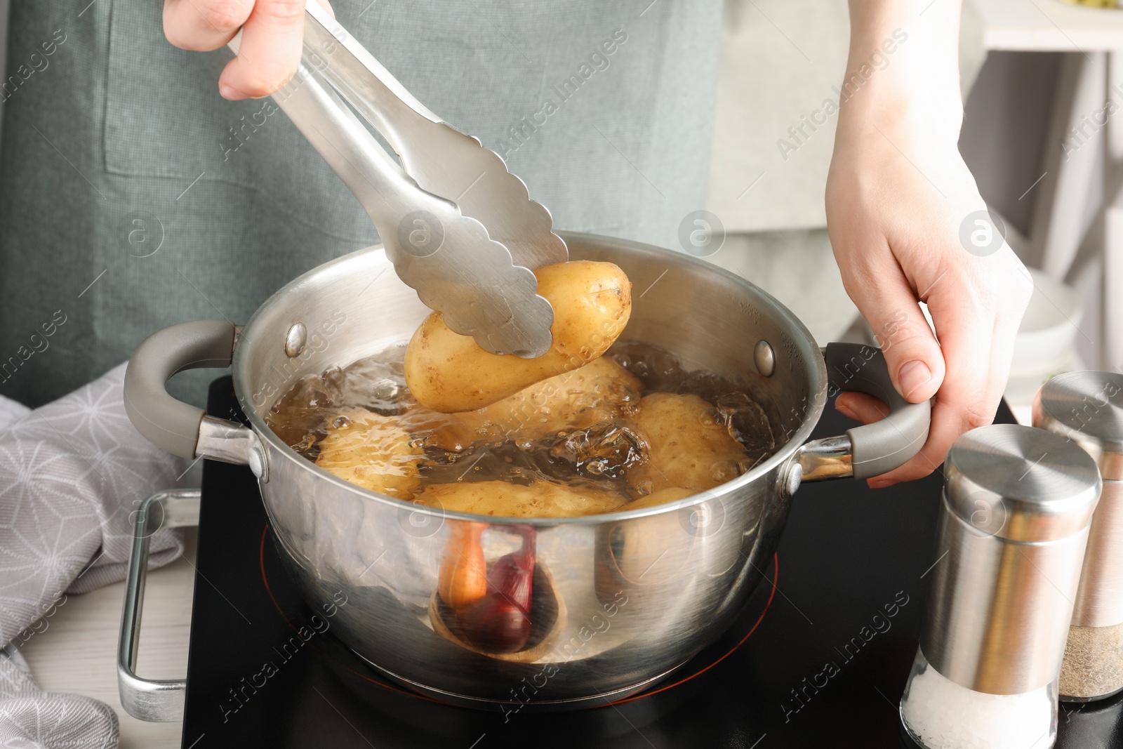 Photo of Woman putting raw potato into pot on stove, closeup