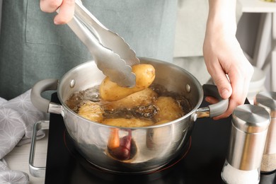 Photo of Woman putting raw potato into pot on stove, closeup